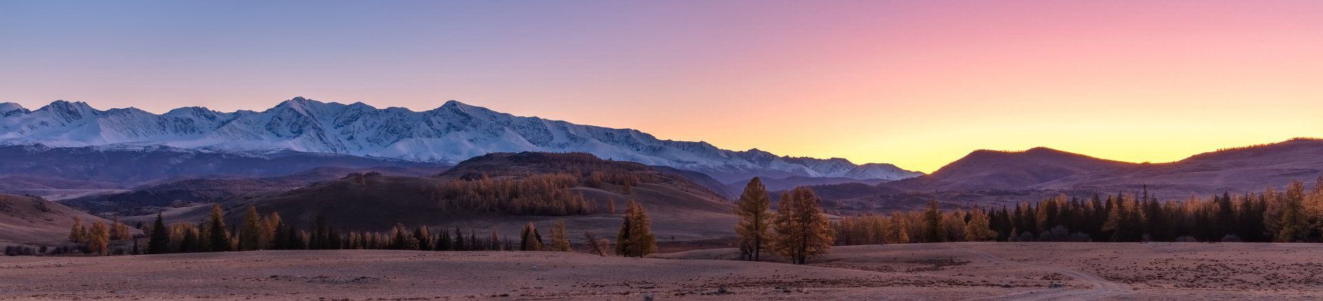 A sunset over a mountain range with trees in the foreground and mountains in the background.