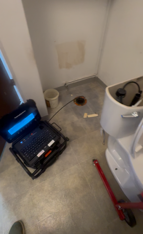 Cluttered utility room with a wet floor, red tool handle, and an open equipment cart near a toilet