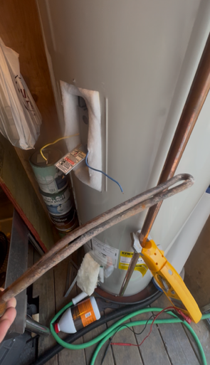 Cluttered utility closet with pipes, hoses, and tools against a wall.