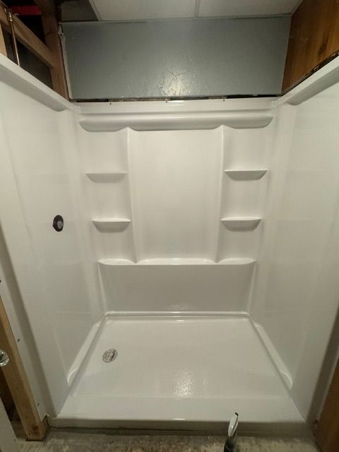 Empty white shower stall with molded shelves, grab bar, and drain