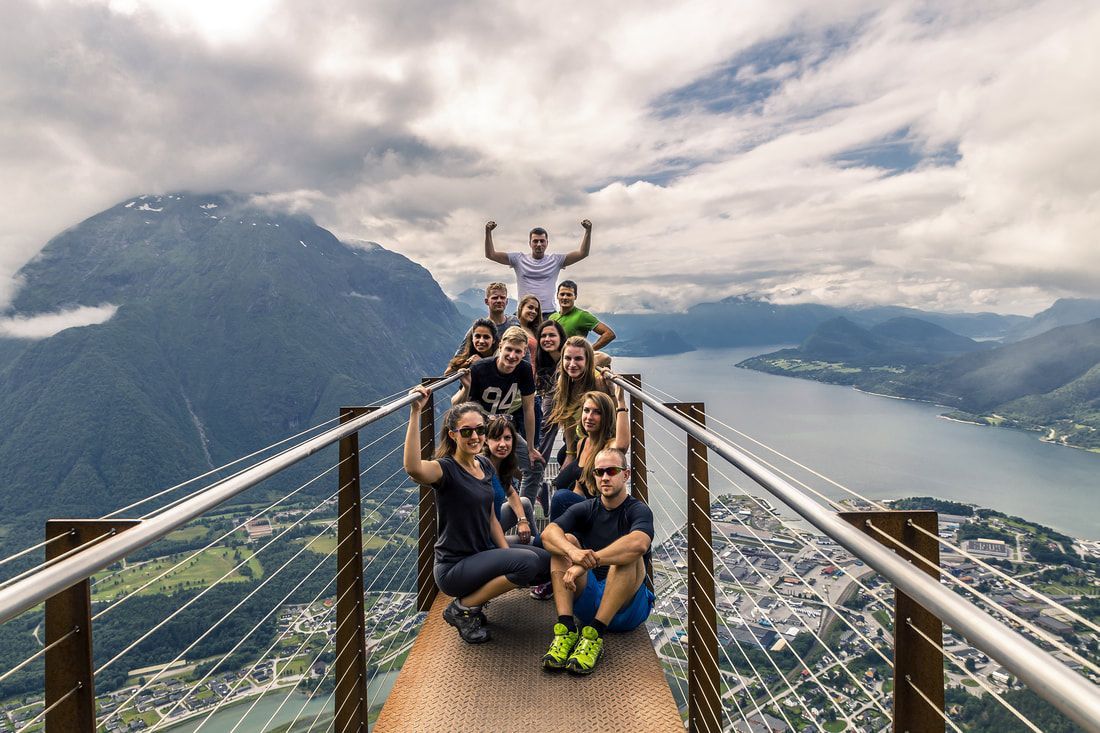 group standing on lookout on a mountain A group of people are posing for a picture on top of a mountain.