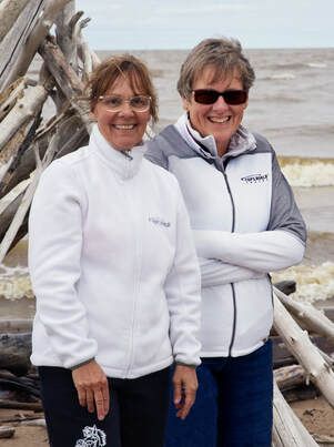 top of the world travel team Two women are standing next to each other on the beach.