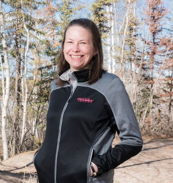 women in black and grey jacket A woman wearing a black and grey jacket is smiling in front of trees