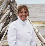 women in white jacket looking at camera A woman in a white jacket is standing in front of a pile of driftwood.