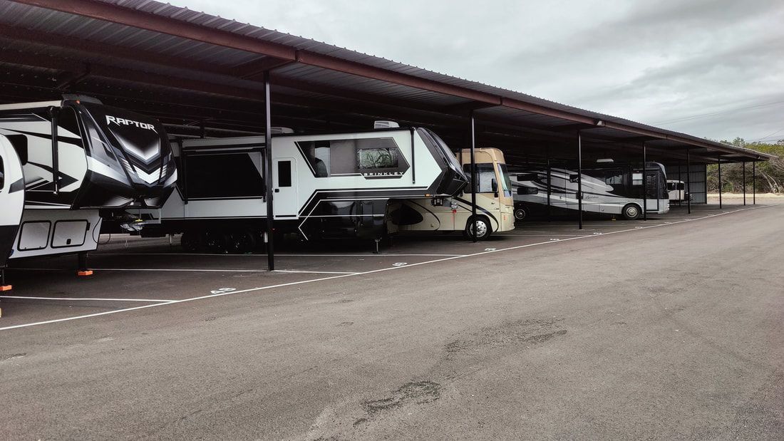 RVs parked under a long metal awning at an outdoor storage facility.