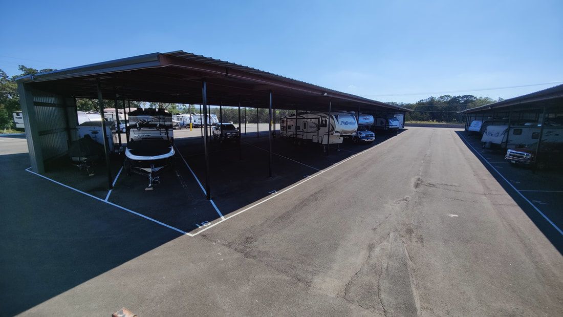 RV storage facility; vehicles parked under a metal roof, asphalt driveway, sunny day.