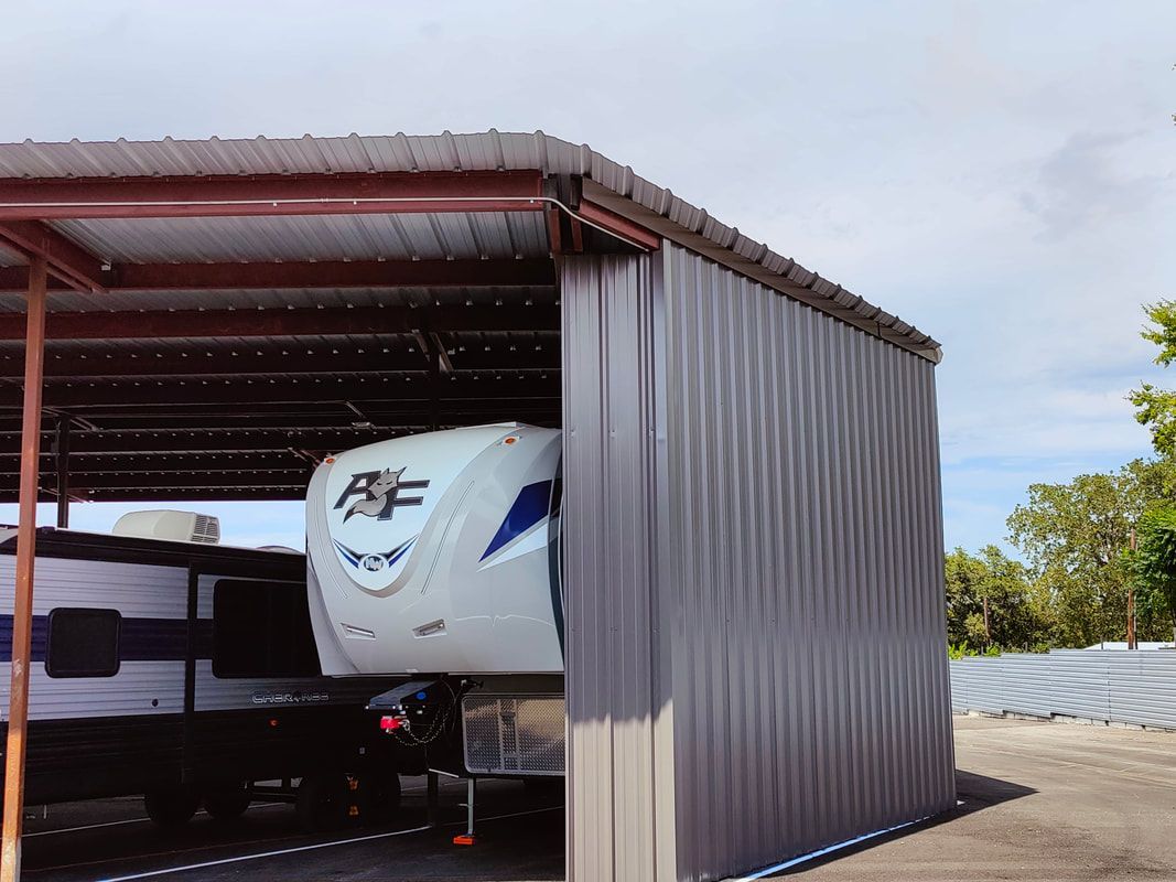 RV parked under a metal carport, with corrugated steel siding.