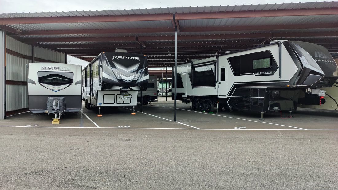 RVs parked under a metal awning at a storage facility.