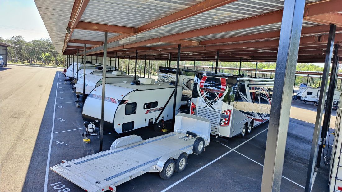 RVs and trailers parked under a covered structure in an outdoor lot.
