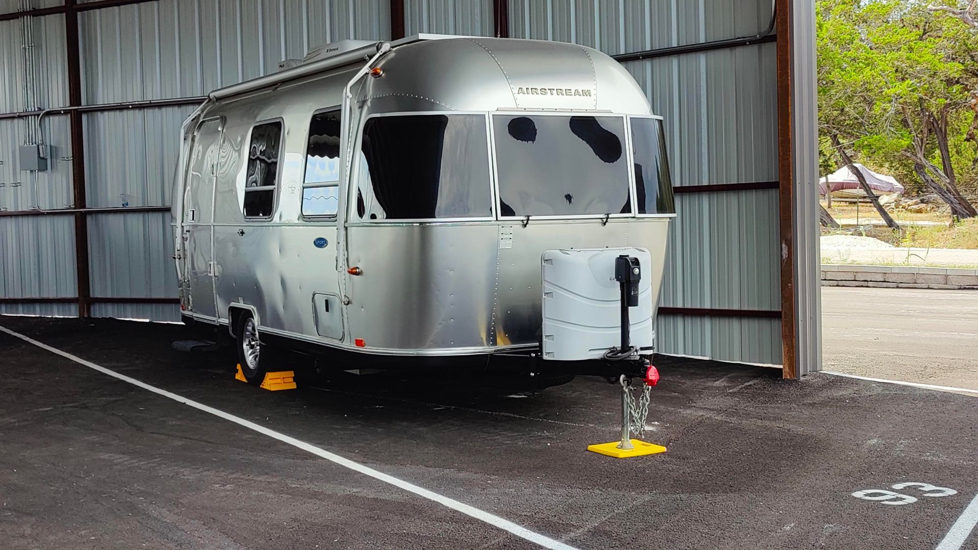 Burned silver travel trailer inside a metal shed, with broken windows and damaged exterior