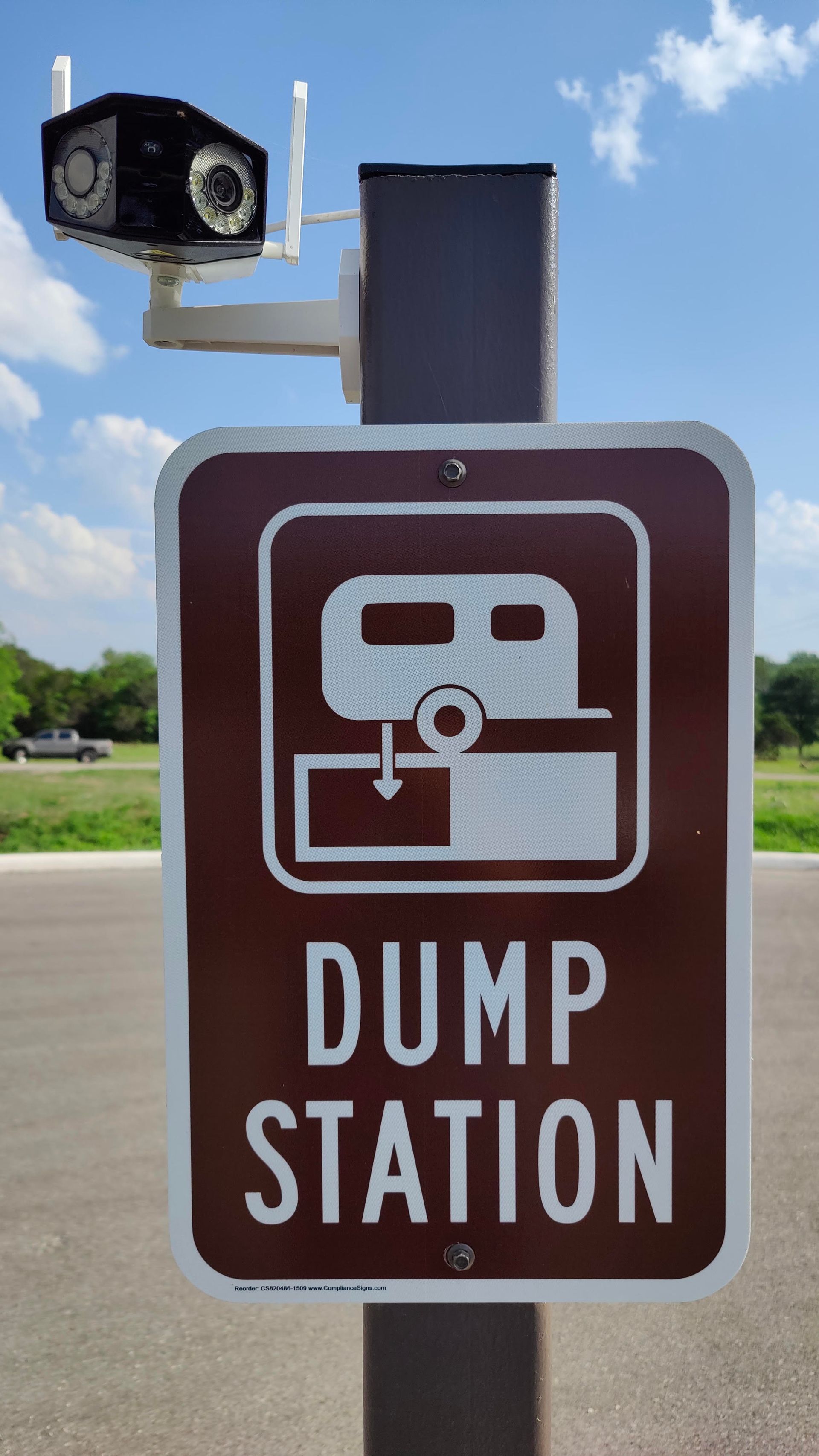 Brown “DUMP STATION” sign with RV icon beside a roadside utility box under a blue sky