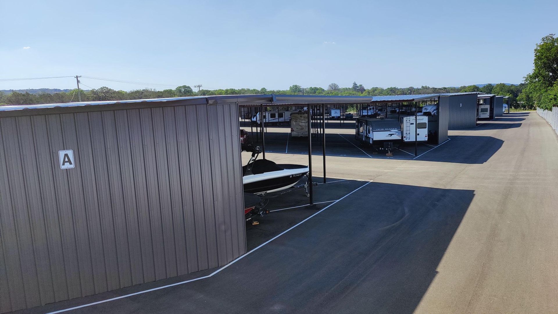 Row of covered outdoor carports beside a paved lot under a clear blue sky