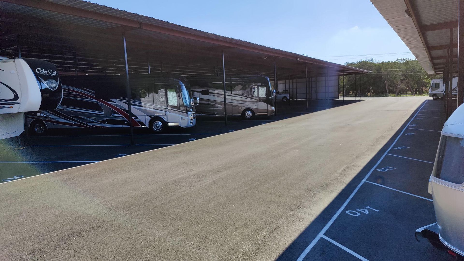 Covered parking lot with several parked cars and a wide sunlit driveway