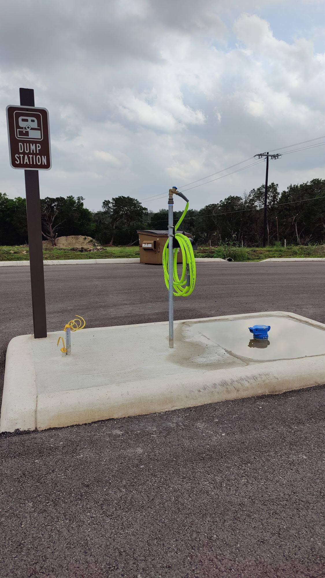 Portable pet wash station with green hose and blue bowl on a concrete pad in a parking lot
