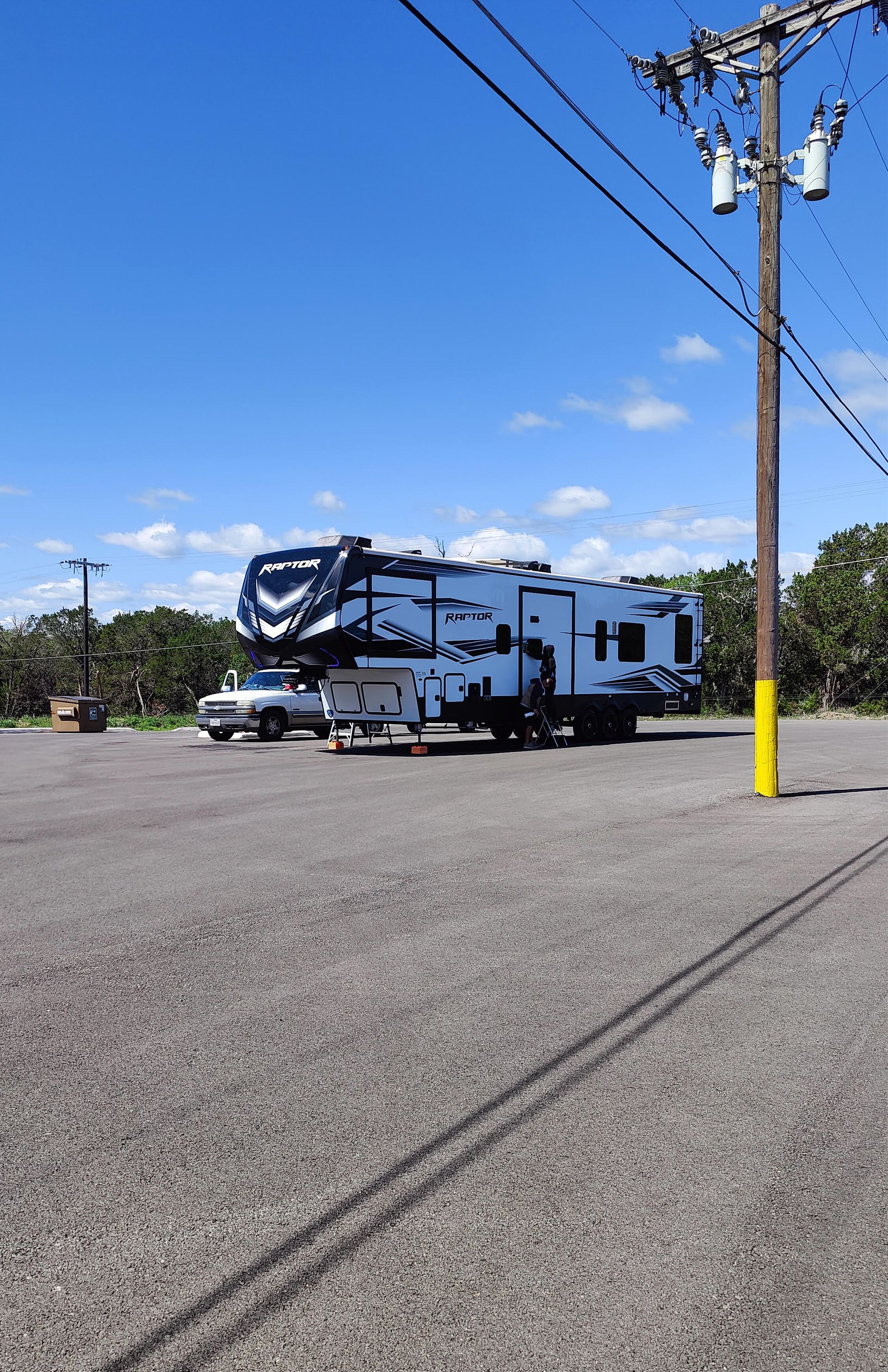 White RV trailer in a gravel lot under a blue sky, with power lines and a utility pole in the foreground