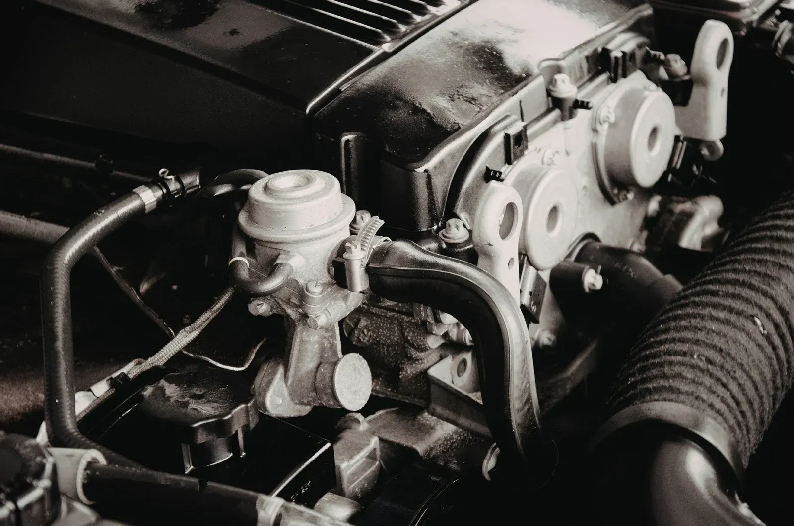 Close-up of a car engine with various metal components and hoses in a monochrome color.