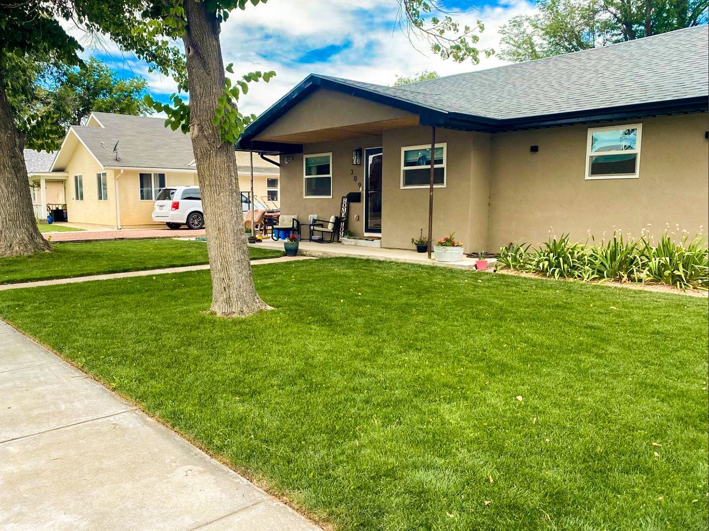 Suburban apartment building with a green lawn, sidewalk, trees, and a covered patio under blue sky