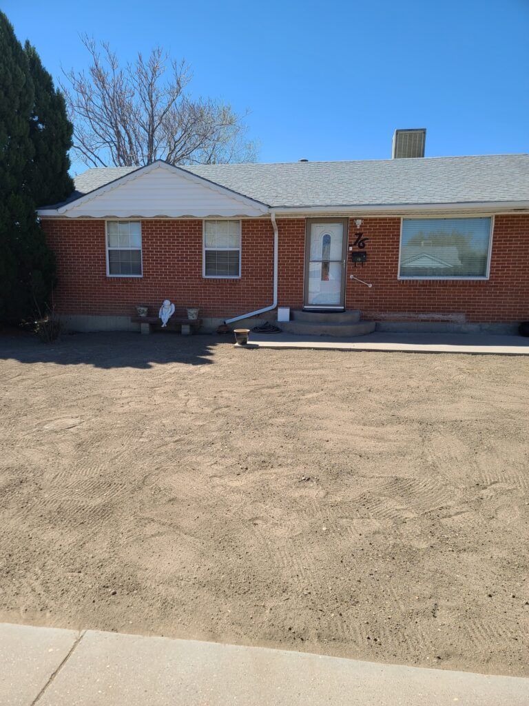 Single-story red brick house with white trim, front porch, and a dry front yard under a clear sky