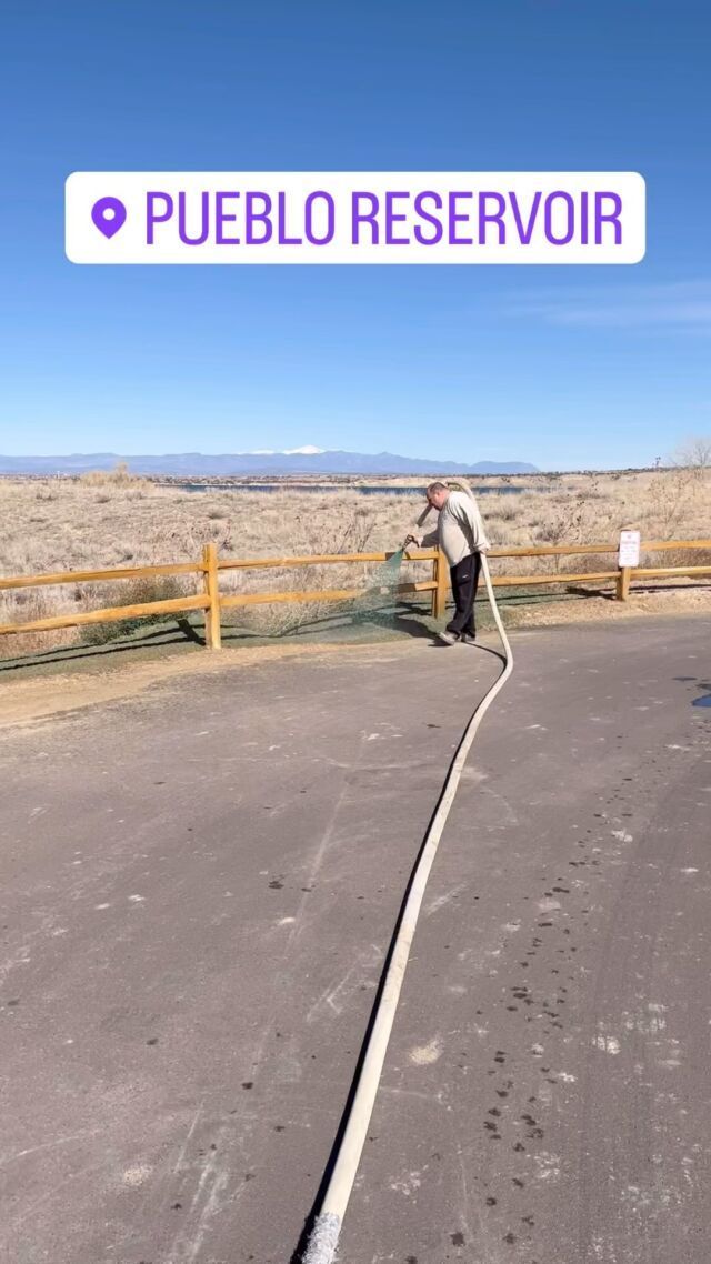 Person holding a hose near Pueblo Reservoir under a clear blue sky.