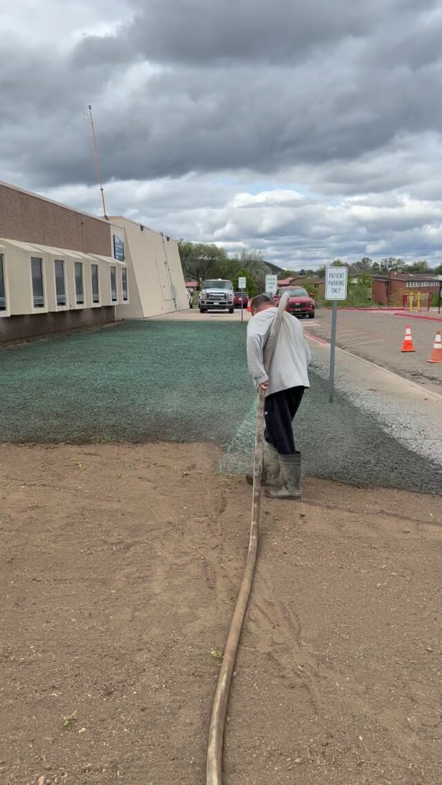 Person in a white coat stands on a gravel path at a construction site under cloudy skies.