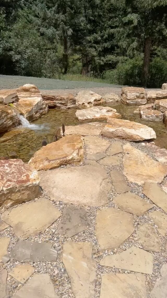 Stone pathway beside a small waterfall, with trees and greenery in the background