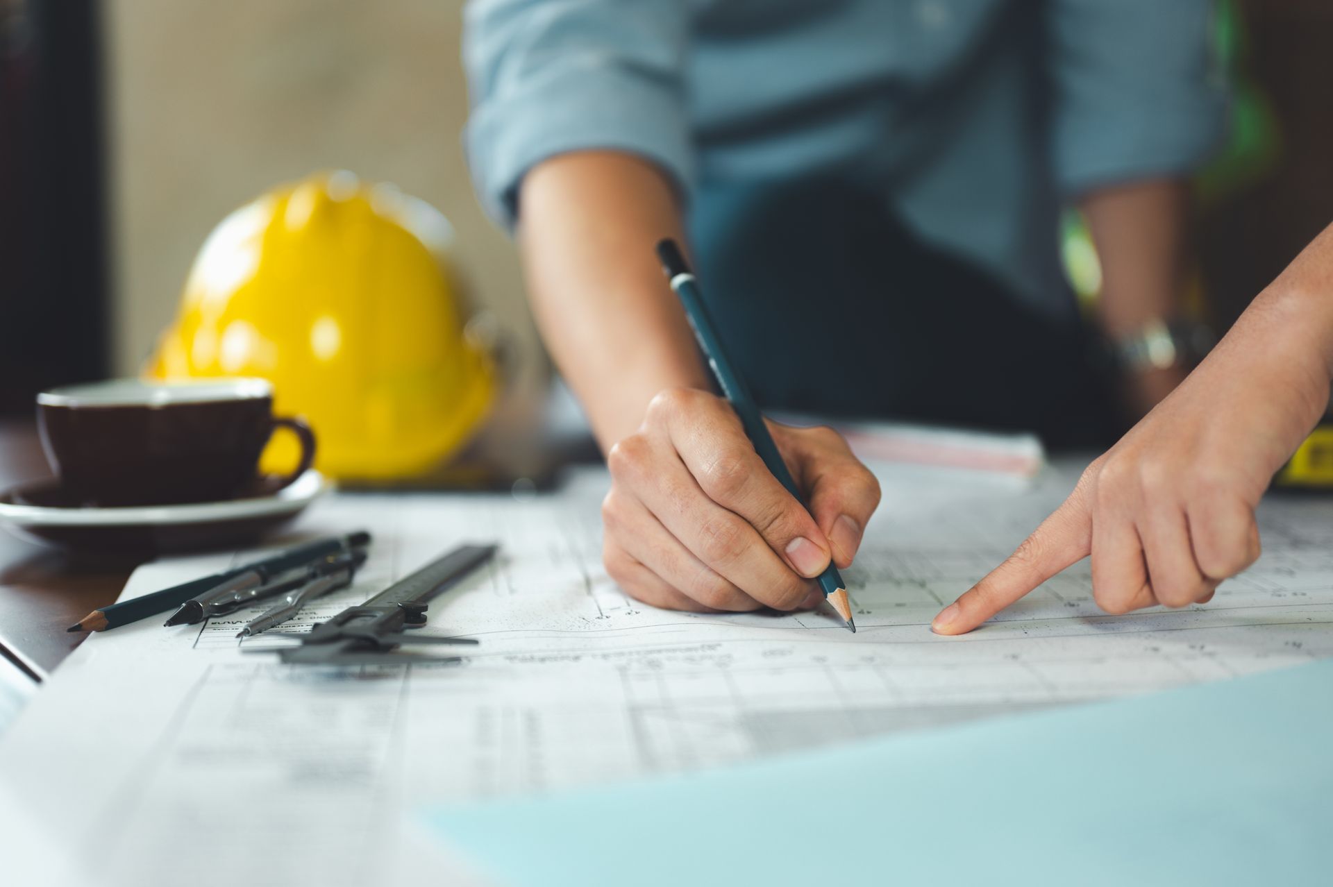 Two people collaborate over construction blueprints, with one drawing and the other pointing at the plans.