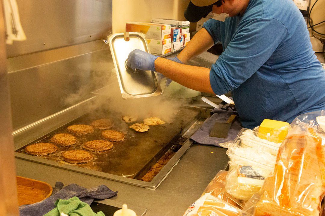 A man is cooking hamburgers on a grill in a kitchen.