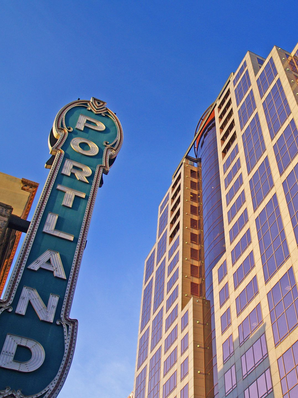 Portland sign beside a tall glass office building against a clear blue sky