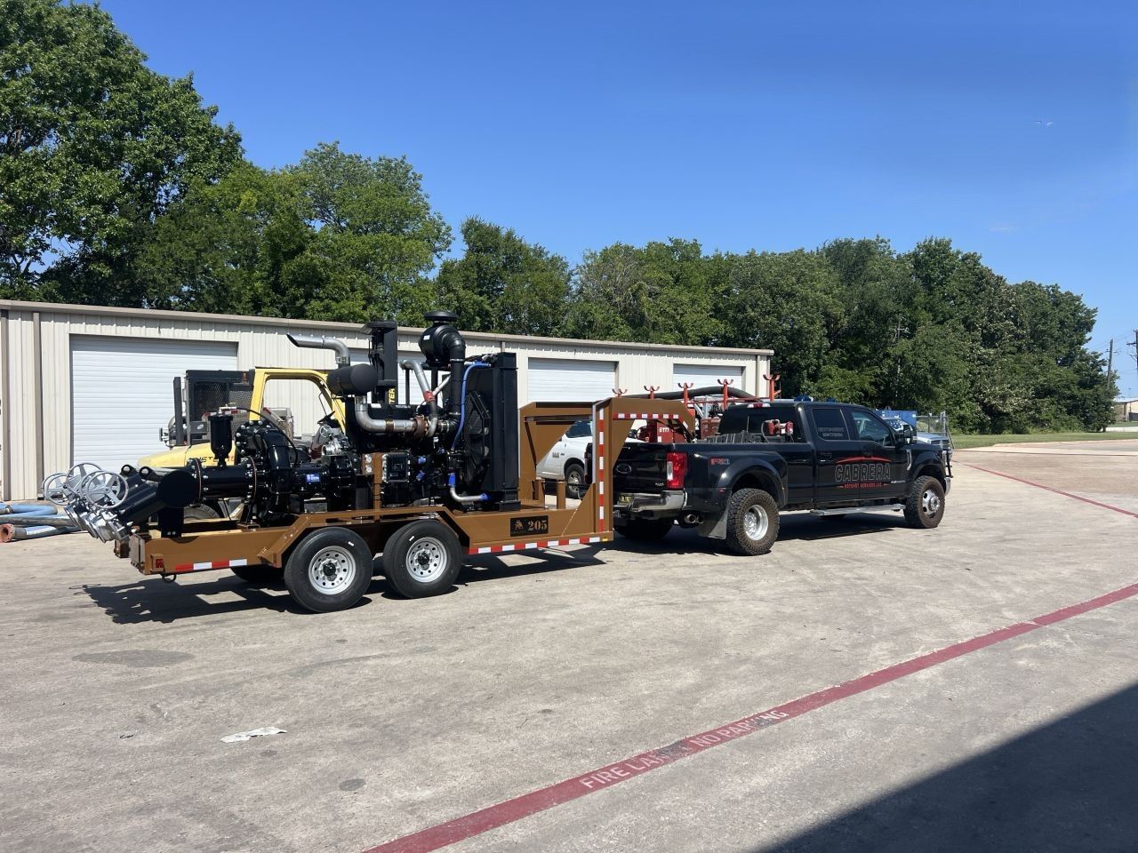 Black pickup truck towing a trailer loaded with construction equipment in a parking lot.