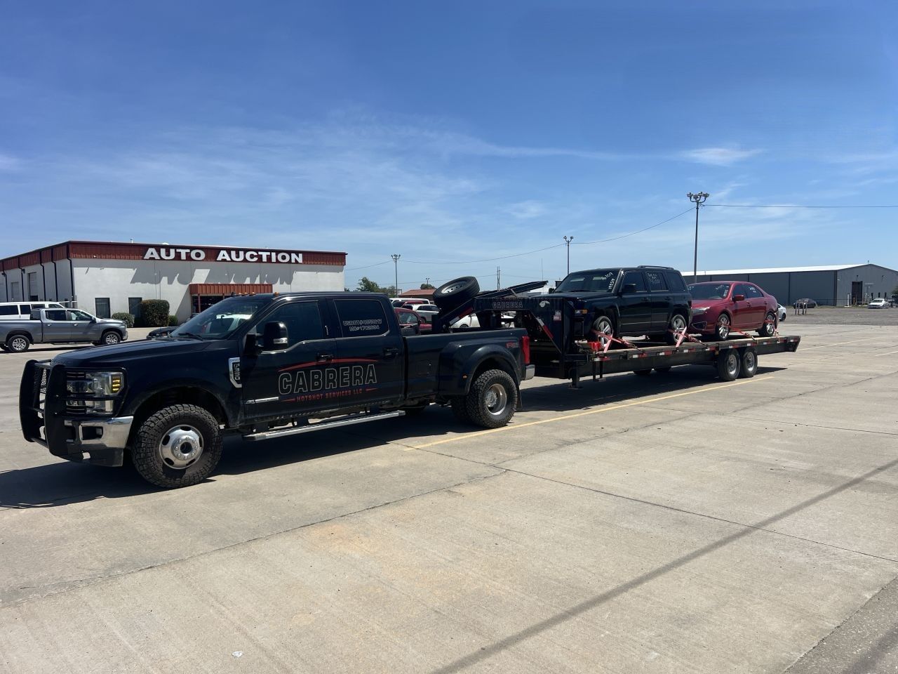 Black pickup truck hauling a red trailer with another truck in a parking lot under a clear sky