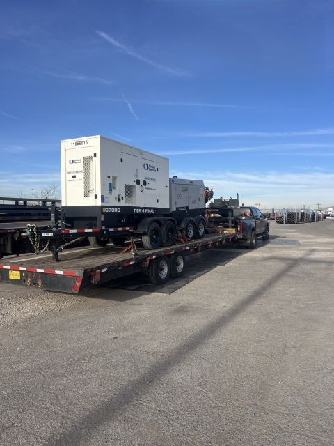White industrial equipment on a flatbed trailer in a parking lot under a clear blue sky.