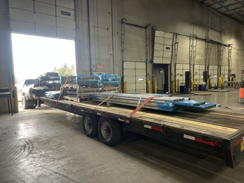 Flatbed trailer loaded with blue metal beams inside a warehouse loading dock