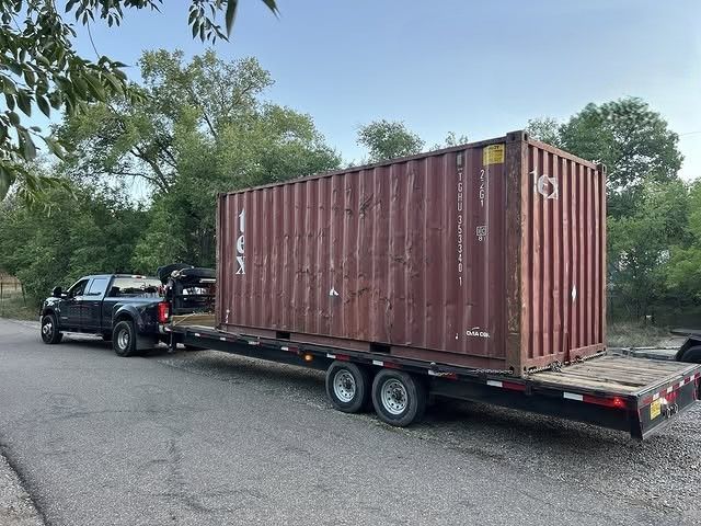 Pickup truck hauling a long flatbed trailer with a shipping container on a roadside