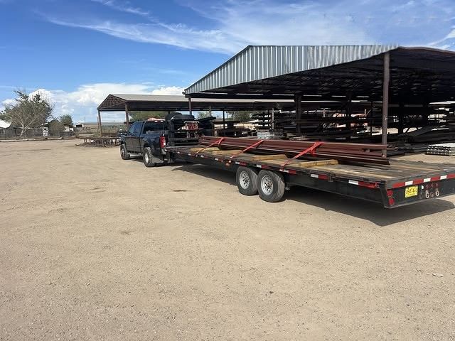 Flatbed trailer loaded with steel roofing panels in a dusty outdoor yard under a blue sky