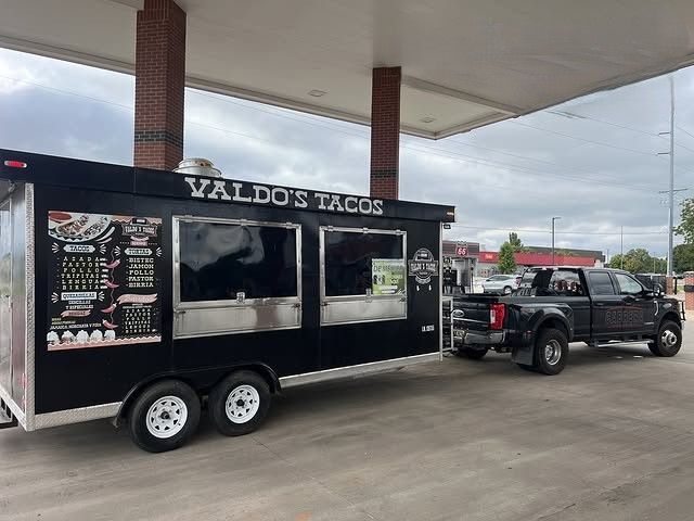 Black taco trailer labeled “Valdo’s Tacos” hitched to a pickup at a gas station