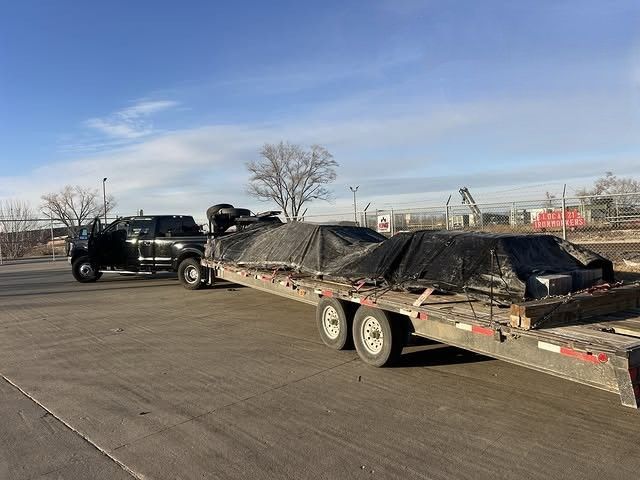 Pickup truck towing a tarp-covered trailer loaded with cargo across a paved lot under a blue sky