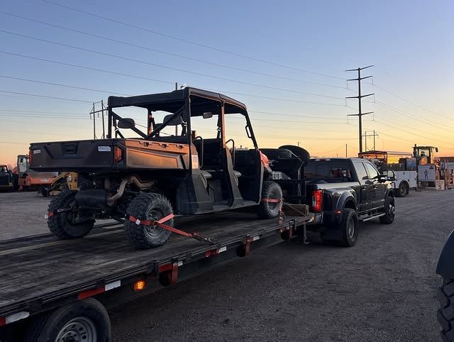 Tow truck hauling a UTV on a trailer at sunset in a parking lot