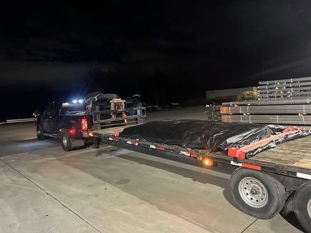 Black pickup towing a flatbed trailer loaded with stacked materials at night in a parking lot