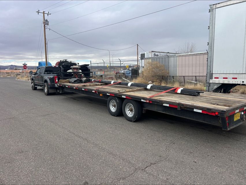 Flatbed trailer carrying equipment parked on a roadside under overcast skies