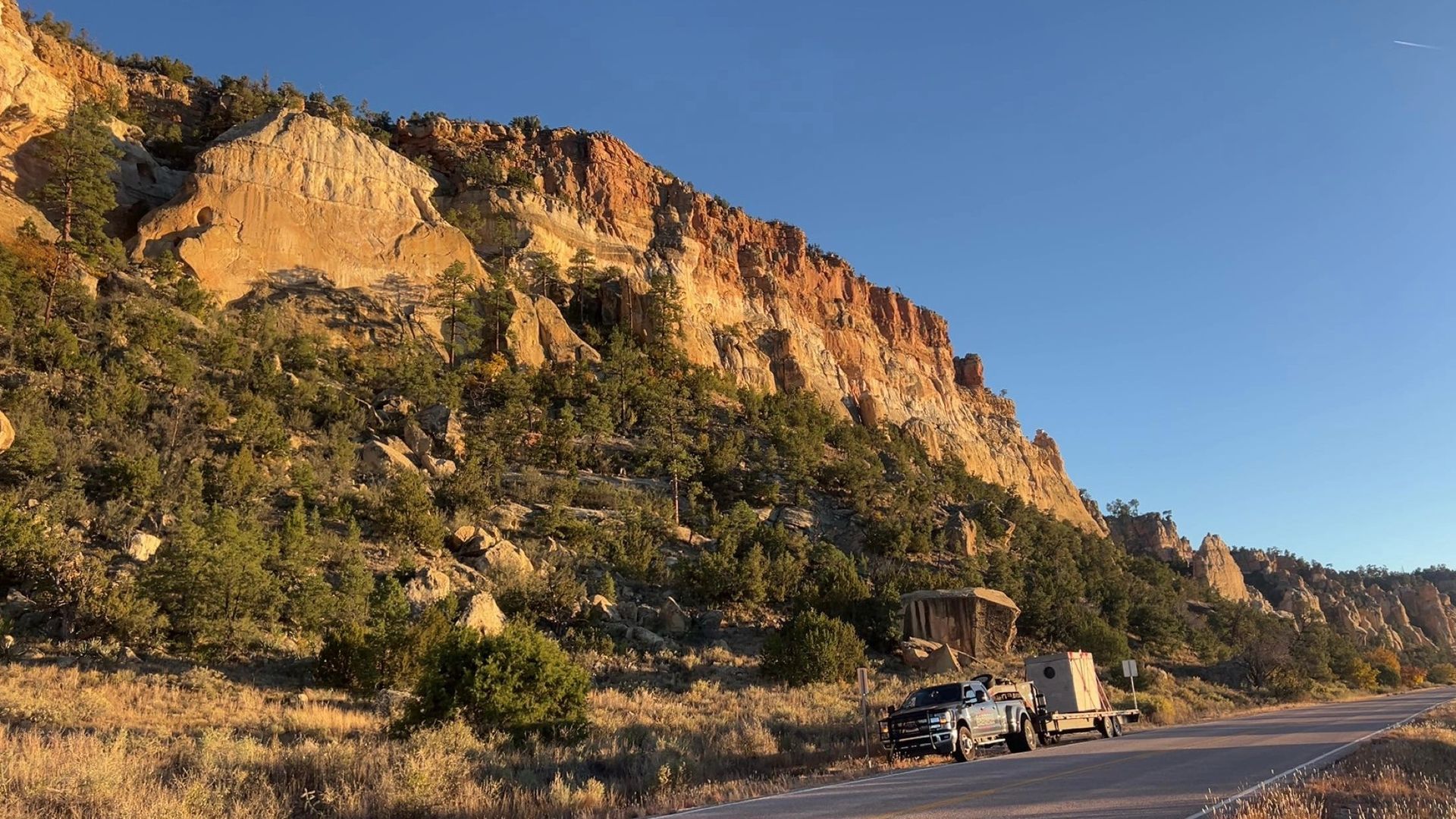 Rocky cliff above a roadside with a parked truck under a clear blue sky