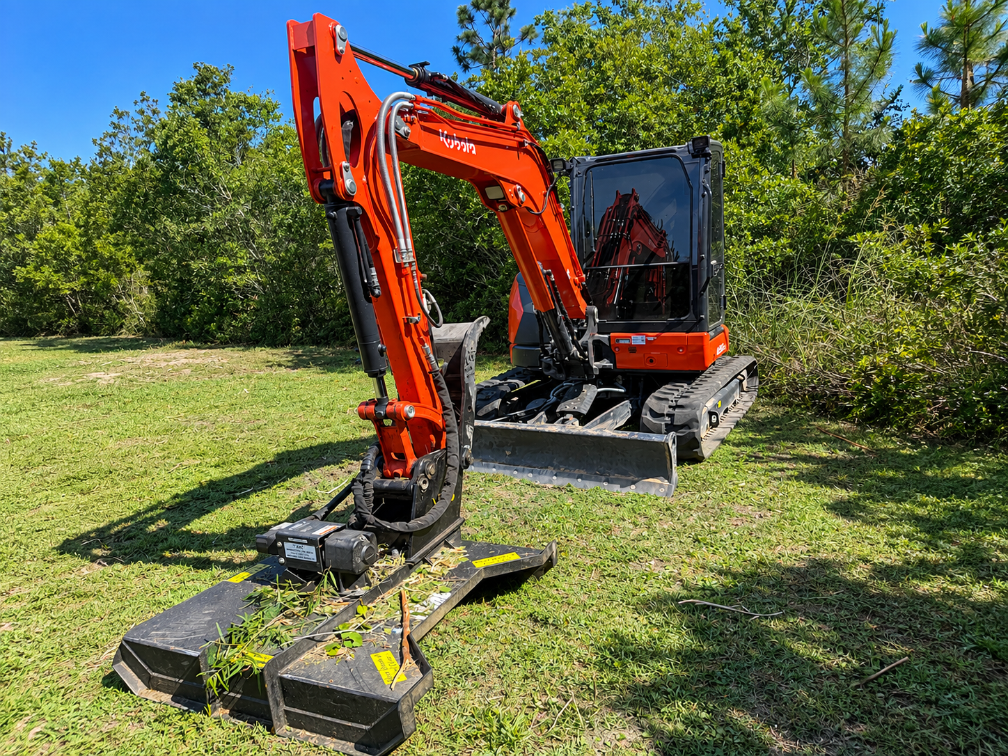 Orange mini excavator mowing grass in a sunny field