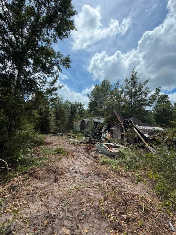 Collapsed structure in a wooded area along a dirt path under a bright, cloudy sky