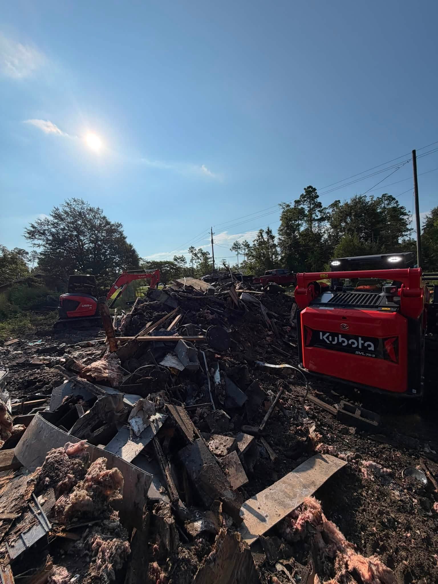 Fire truck beside a pile of burned debris under a bright blue sky