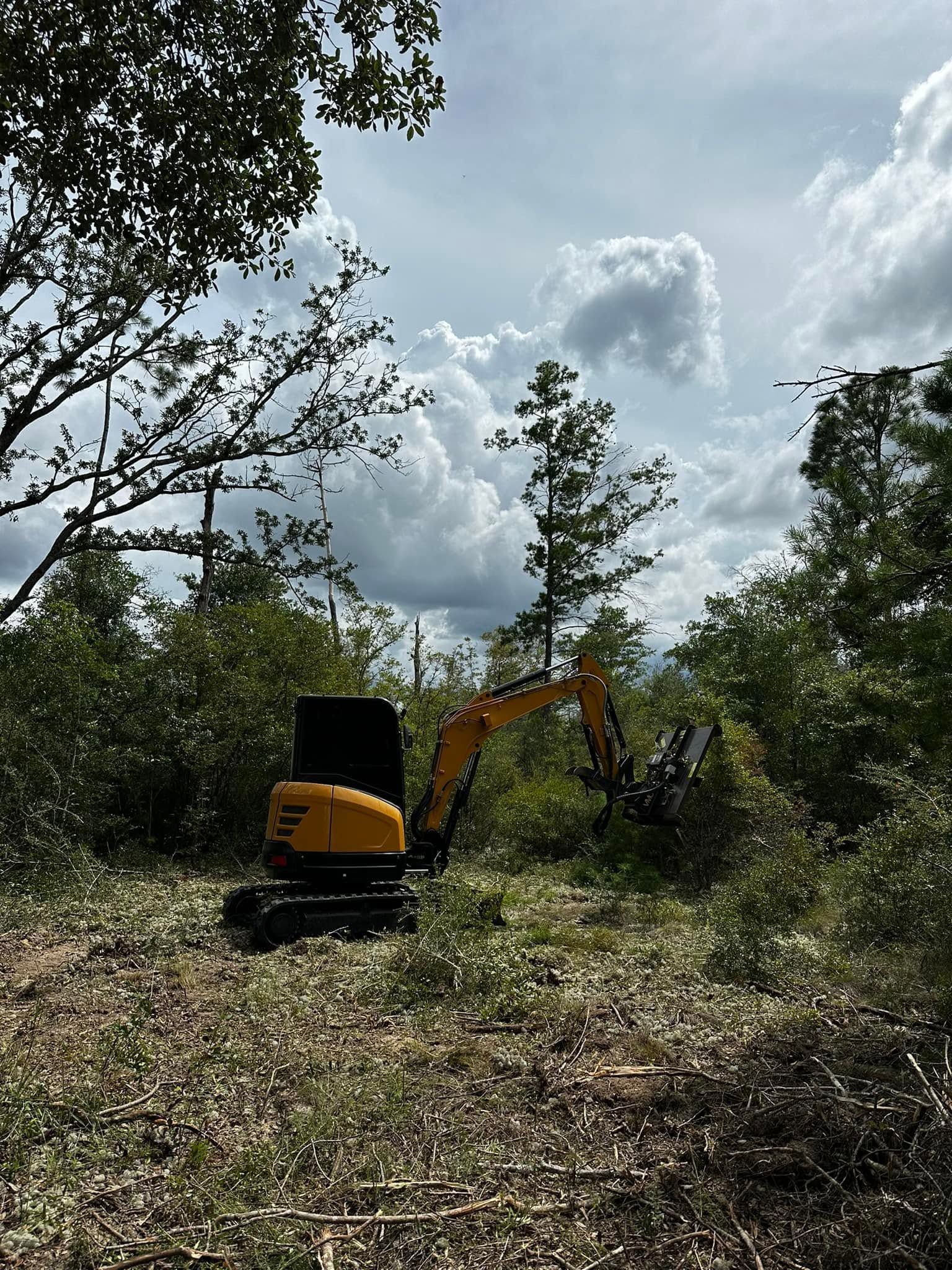 Yellow excavator in a field clearing brush under a cloudy sky