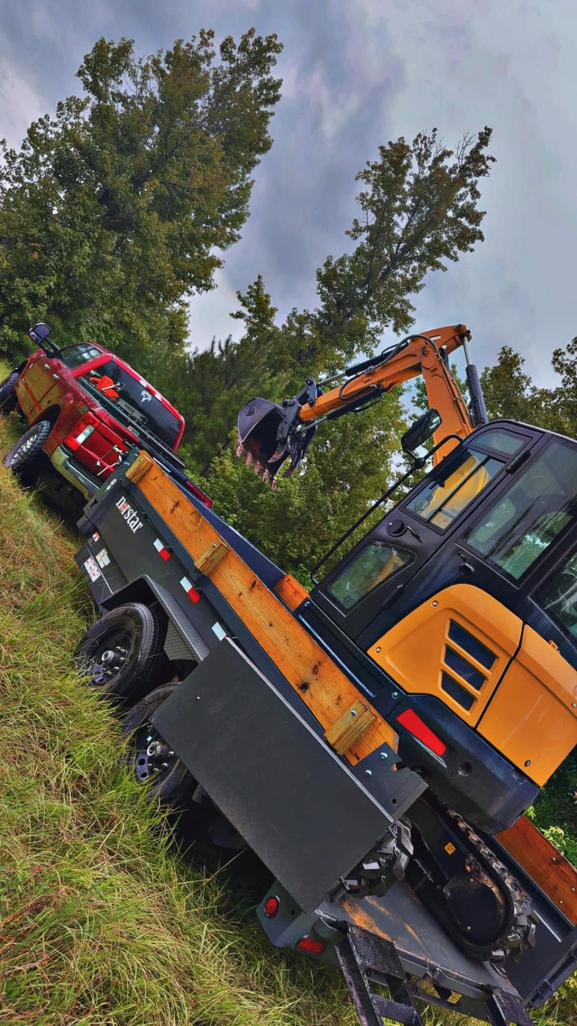Orange excavator beside a red truck on a tilted roadside, with trees and cloudy sky behind them