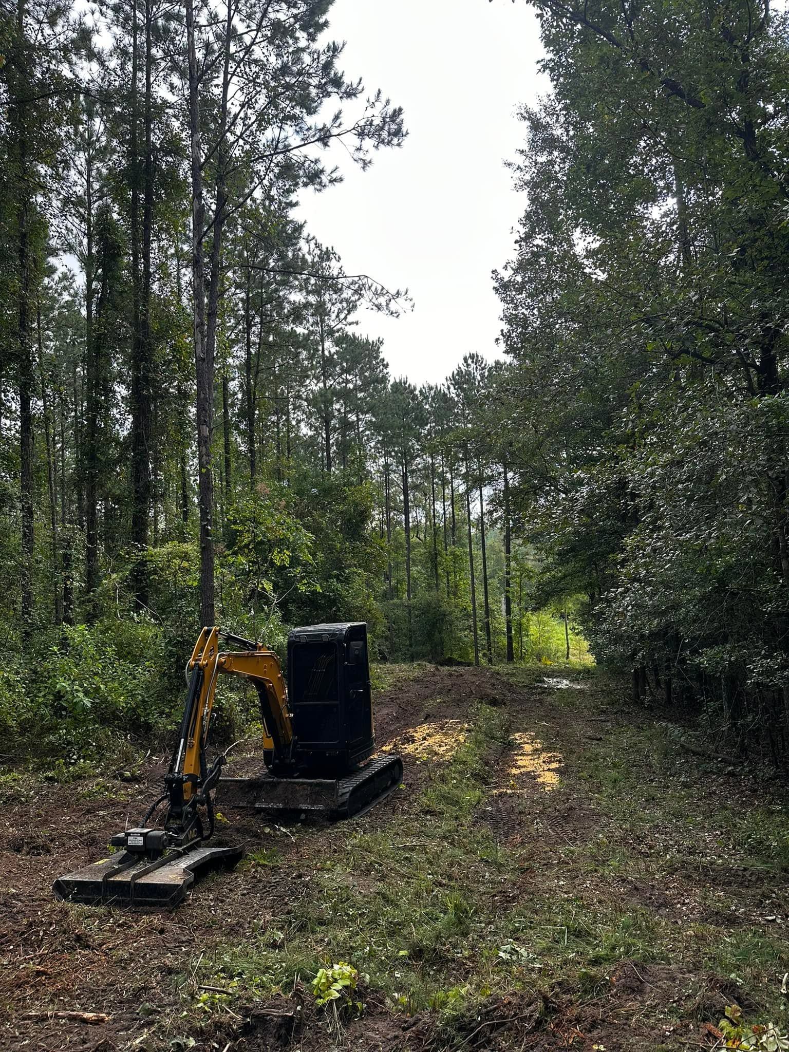 Small excavator clearing a forest path with a dirt mound in the foreground