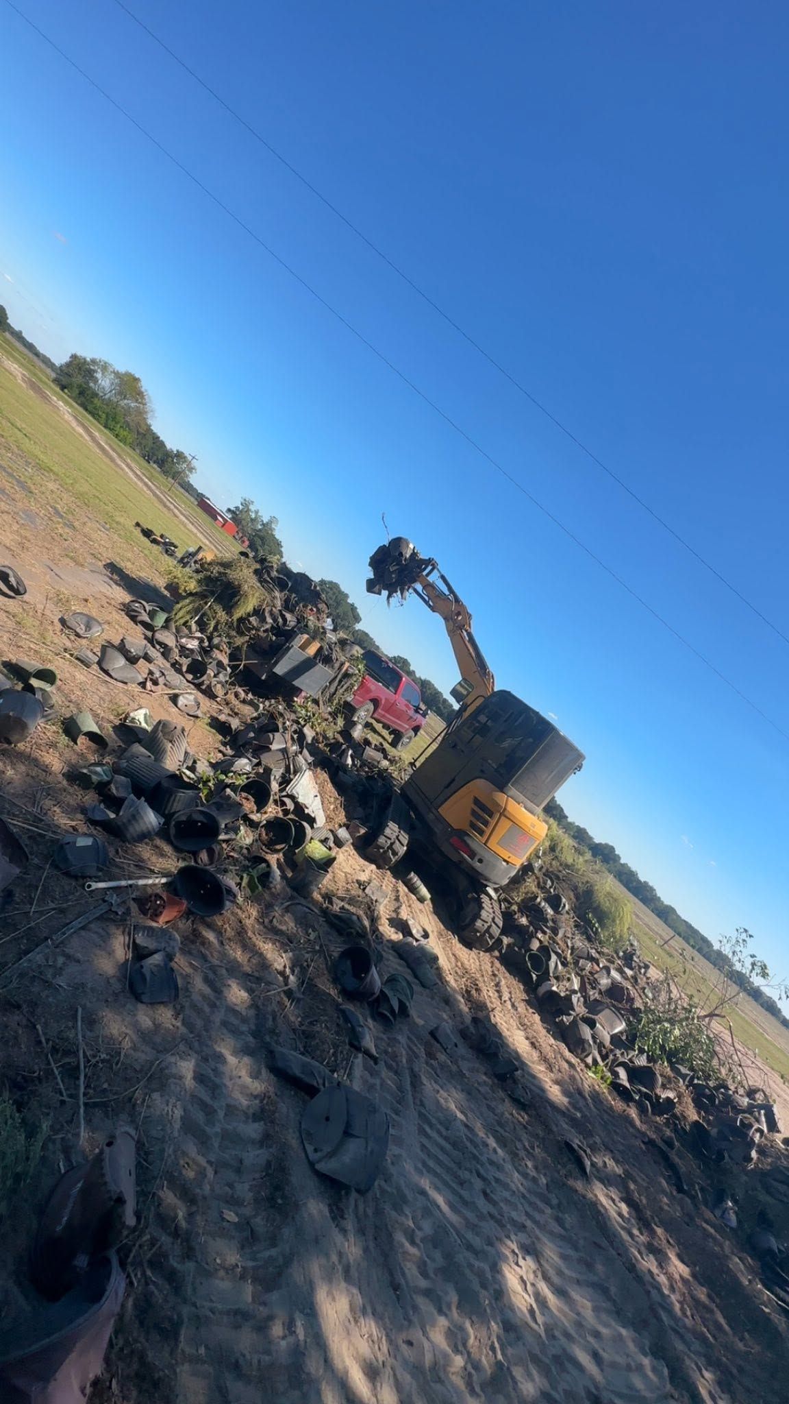 Yellow excavator clearing dirt beside a field under a clear blue sky, viewed at an angle.