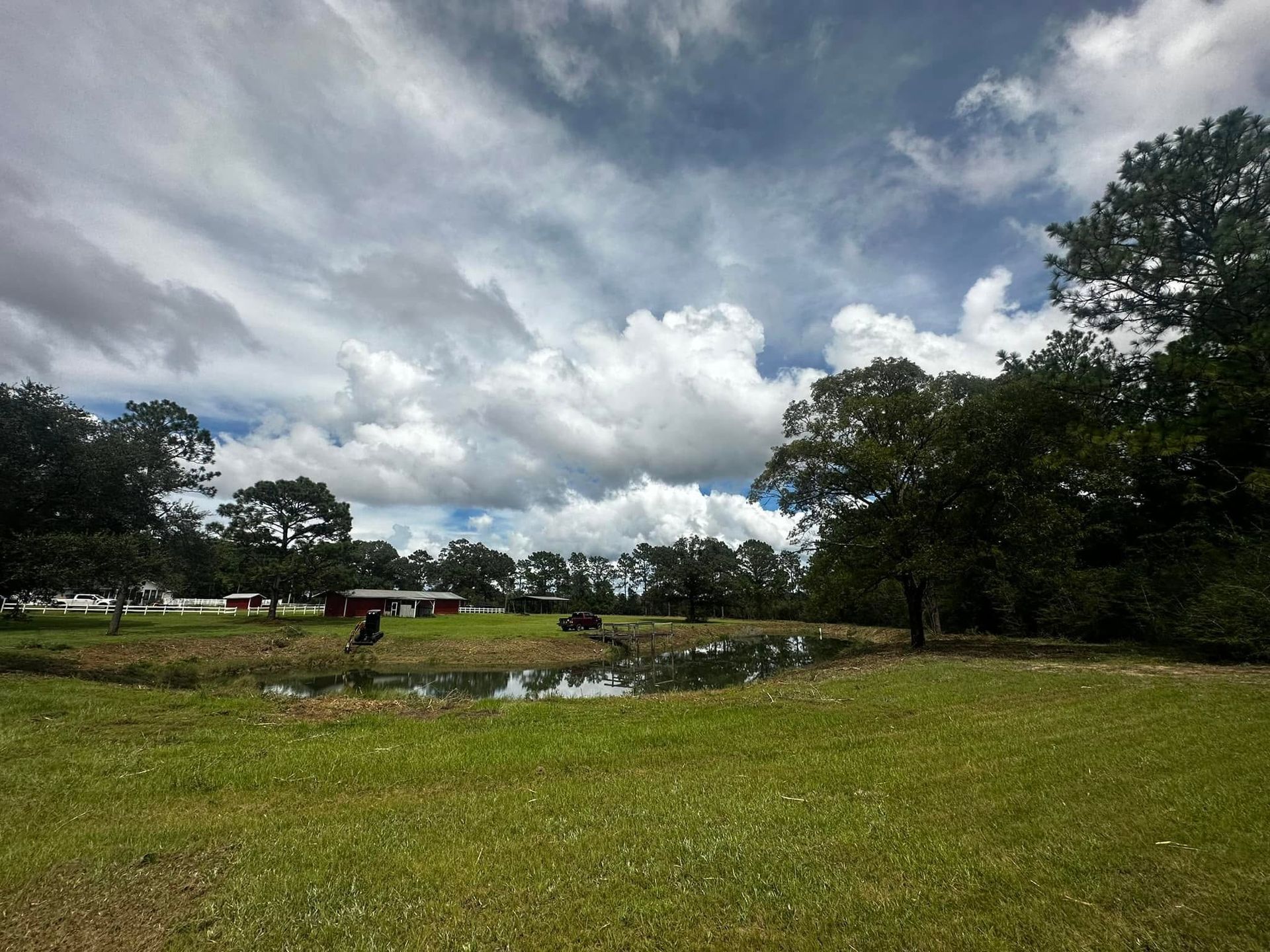 Grassy field with a small pond, trees, and a cloudy sky over a park-like landscape