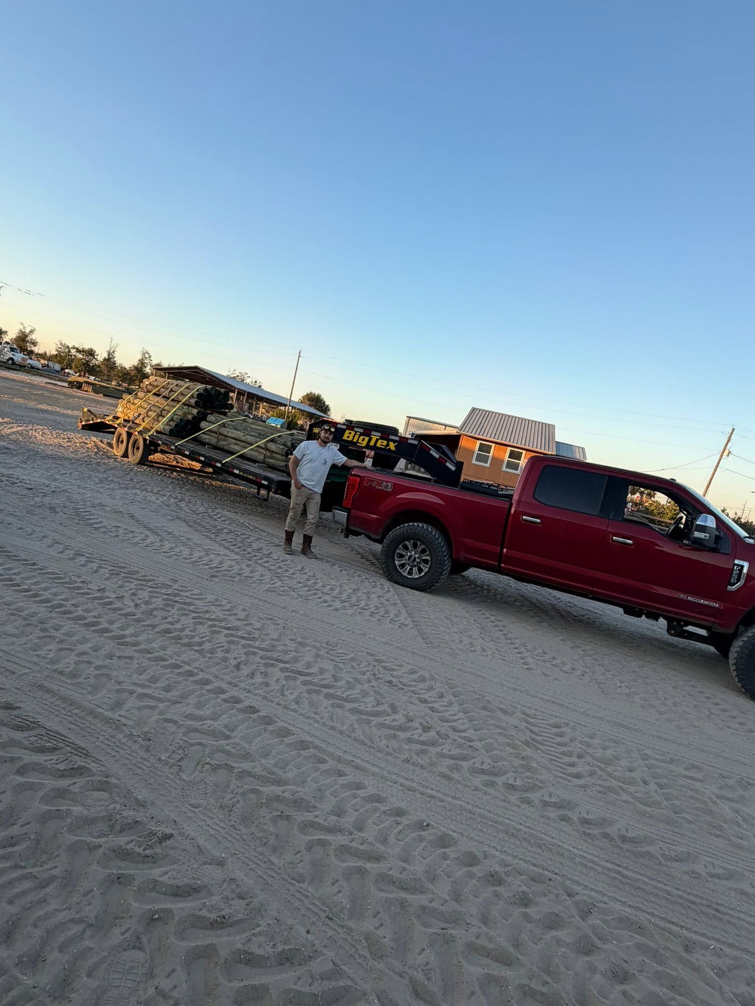Red pickup truck parked on a sandy beach at sunset, with a person standing nearby.