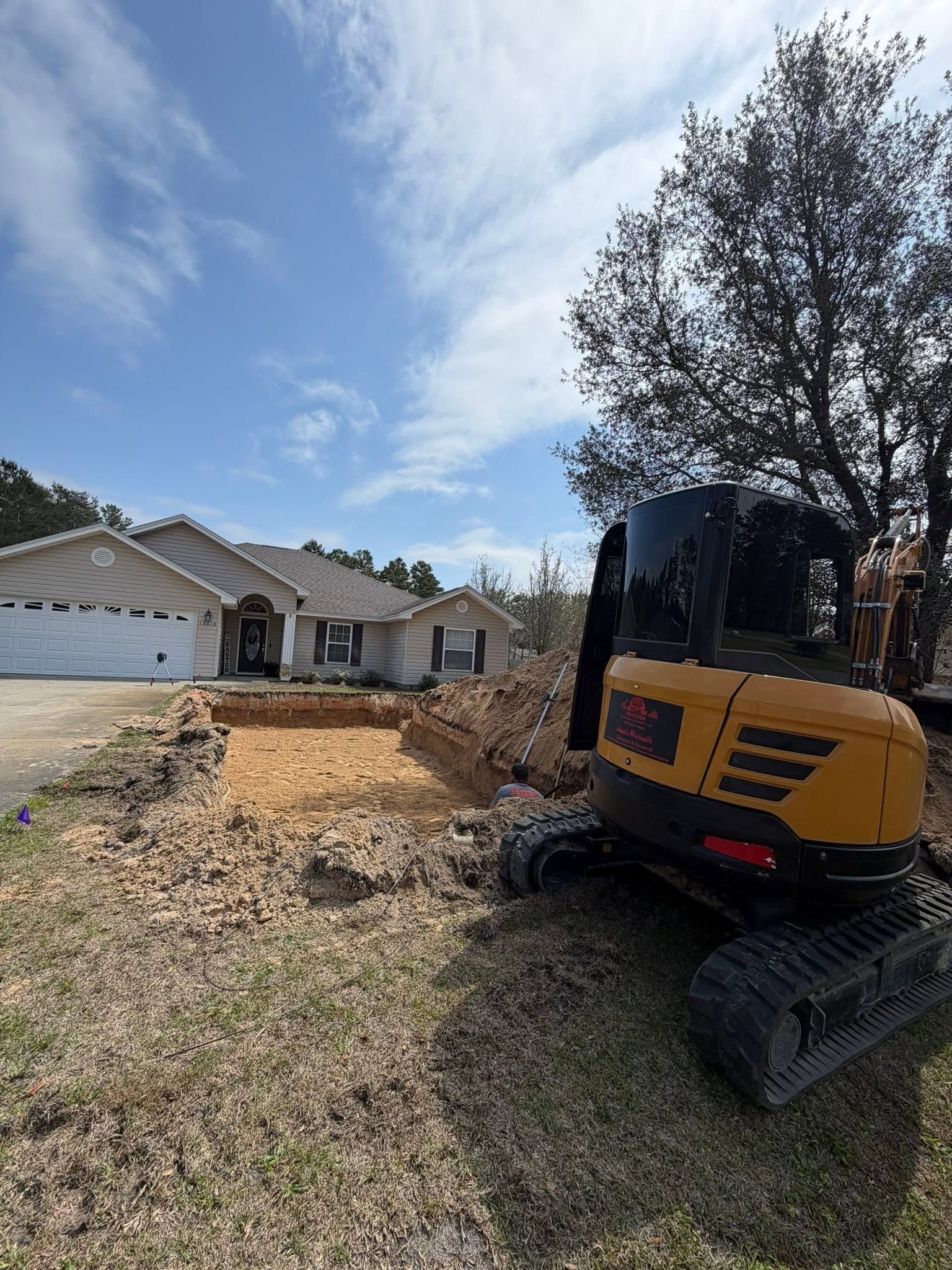 Yellow excavator in a residential yard beside a house under a bright blue sky.